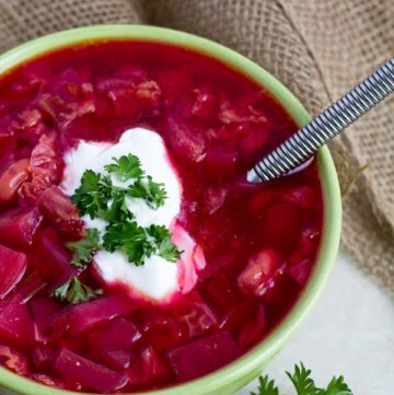 Red beet soup topped with parsley served in a bowl.