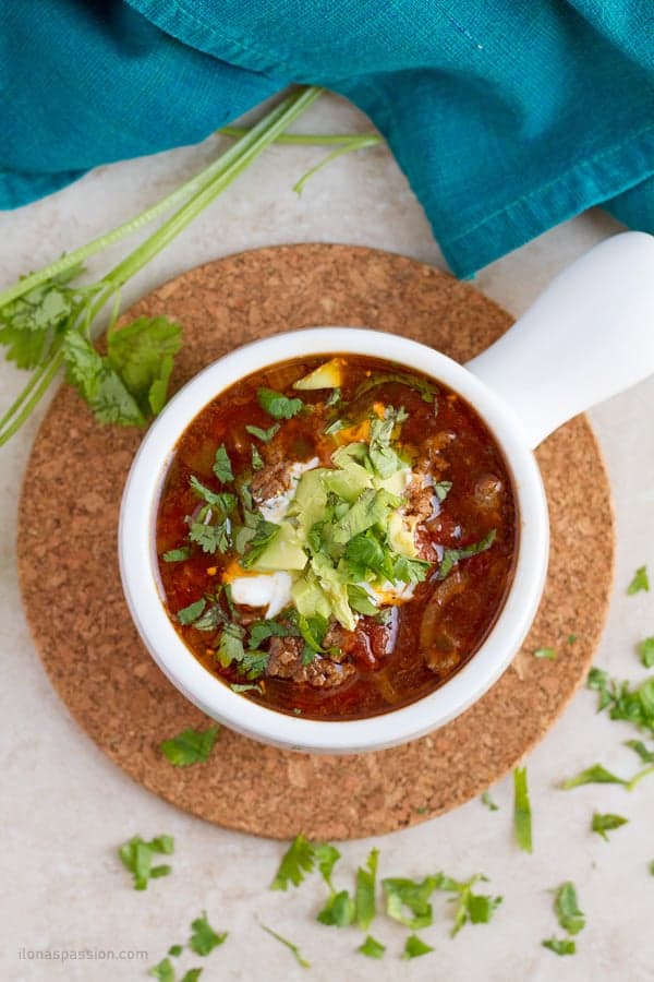 Mexican flavored soup in a white bowl with toppings with cilantro around it.