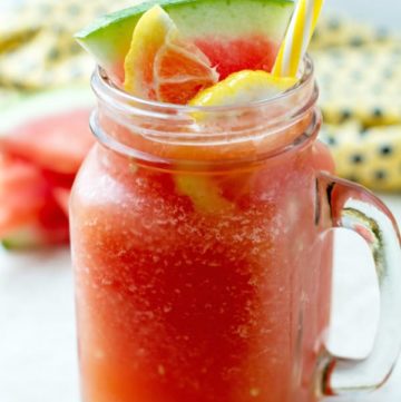 Blended watermelon in a large glass with yellow straw and few pieces of watermelon wedges behind it.