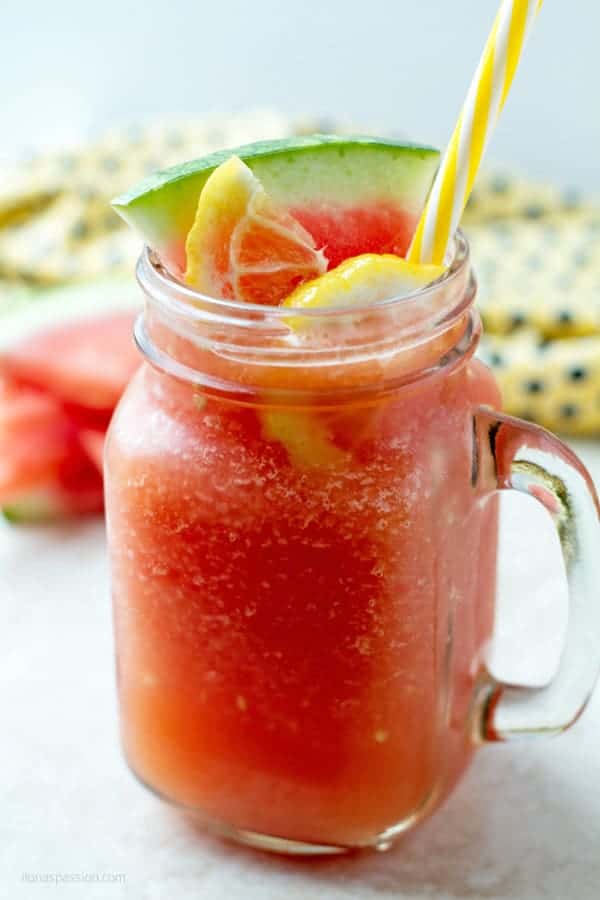 Blended watermelon in a large glass with yellow straw and few pieces of watermelon wedges behind it.