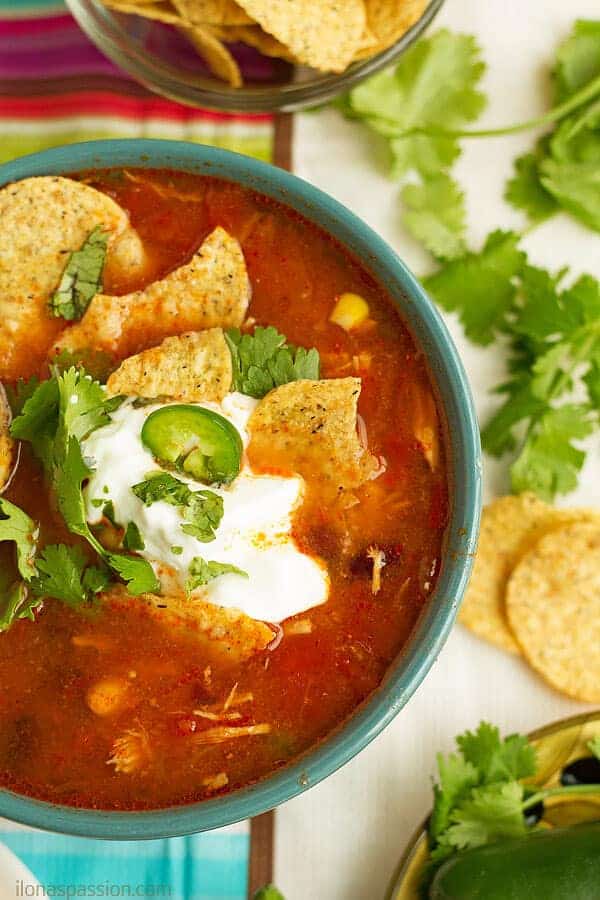 Bowl of taco chicken soup topped with jalapeno, cilantro and tortilla chips made easily in crockpot.