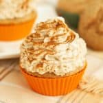 A very close up photo of churro cupcakes with nascarpone frosting and sprinkled with fresh cinnamon in orange silicone liner.