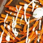 Lots of fries made out of carrots, baked on baking sheet, seasoned with garlic, salt and pepper, a spoon with greek yogurt dip.