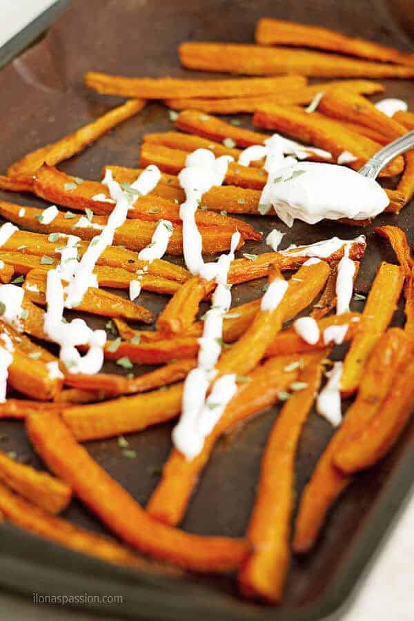 French Fries made of carrots baked on cookina mat and baking sheet topped with greek yogurt dip and sprinkled with basil.