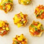 A close up photo off tostitos with mango, tomatoes, cilantro and red onion. Few mini apps around the photo.
