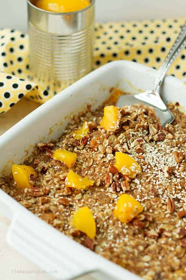 A spoon dipped in peach crumble made with coconut sugar, oats and sesame seeds. Canned peaches in the back.