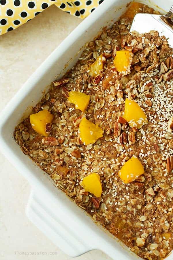 An overhead photo of peach crumble in white baking pan. Baked crumble with some canned peaches on top.