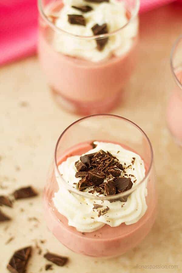 A close up photo of panna cotta in elegant glass in strawberry flavor in color pink with a little cream and sprinkles of chocolate.