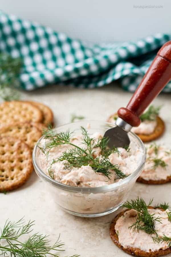 A fish and cream cheese spread in a glass bowl with a knife, few crackers behind it.