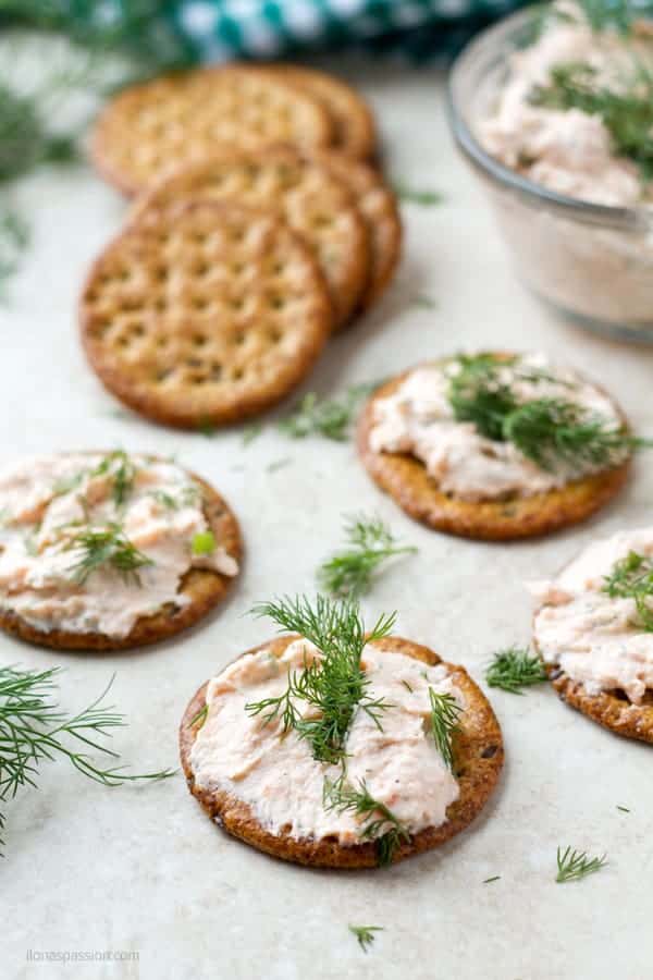 A cracker with cream cheese dip decorated with fresh dill, few plain crackers in the back.