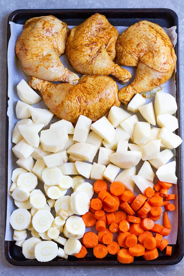Unbaked 4 chicken legs with carrots, potatoes on sheet pan.