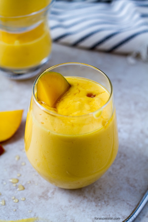 Mango smoothie in a glass with piece of mango.