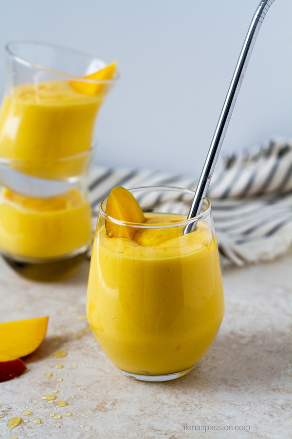 Sweet mango lassi drink with turmeric, milk and yogurt with a straw.