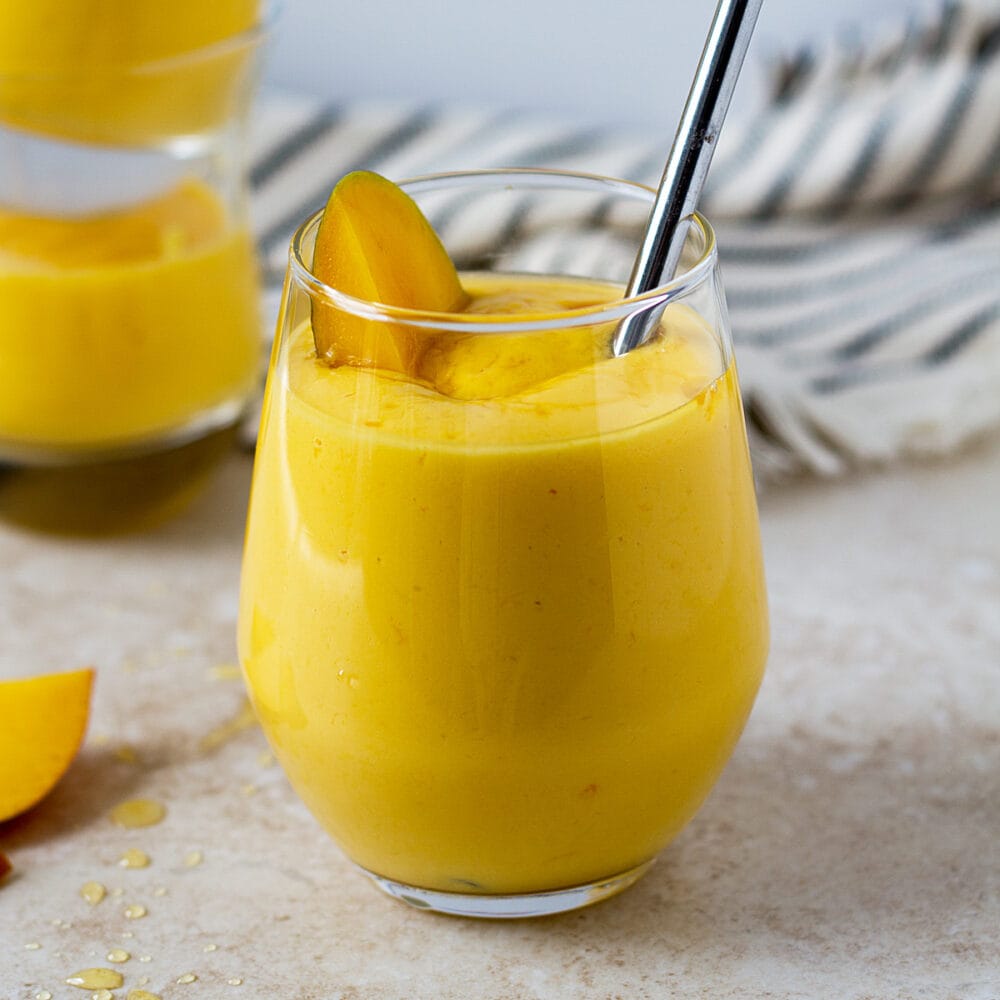 Thick mango lassi in a glass with piece of mango.