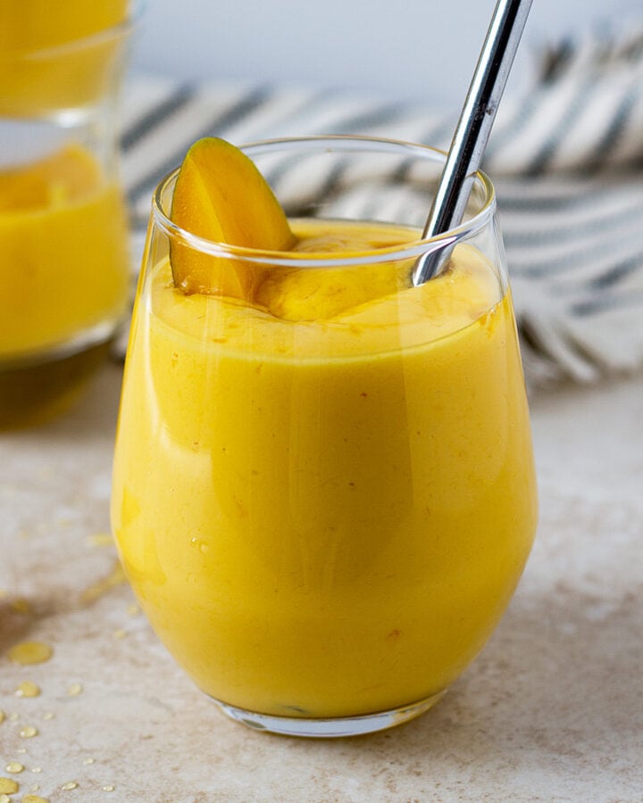 Thick mango lassi in a glass with piece of mango.