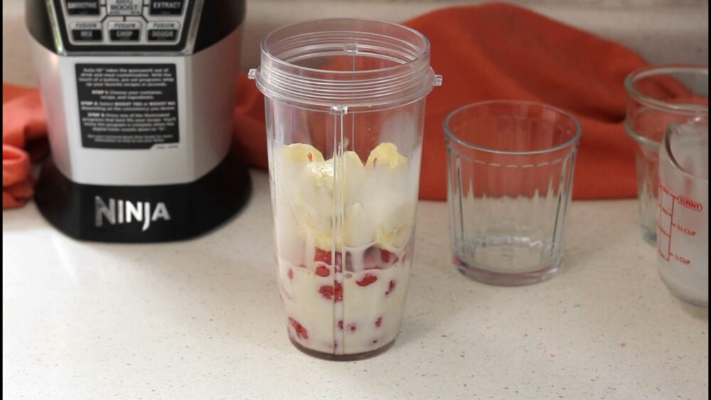 Fruits and plant based milk in a cup, blender in the background.