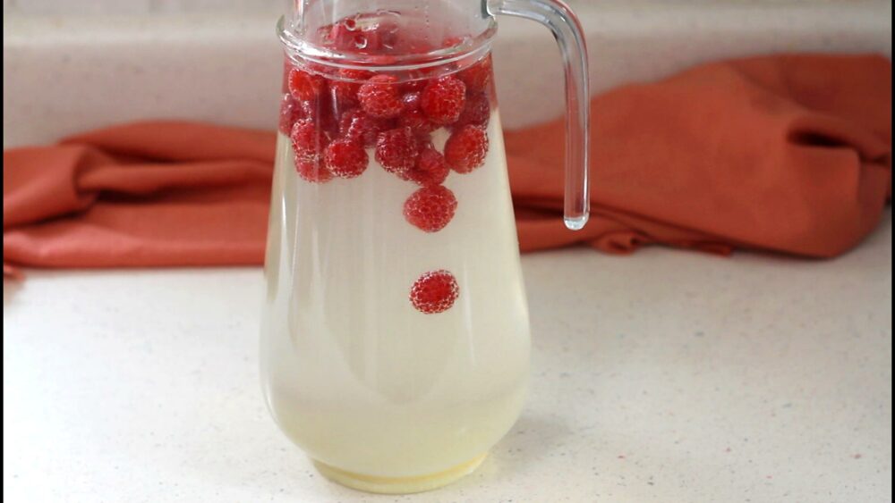 Jar with honey lemonade water and fresh raspberries.