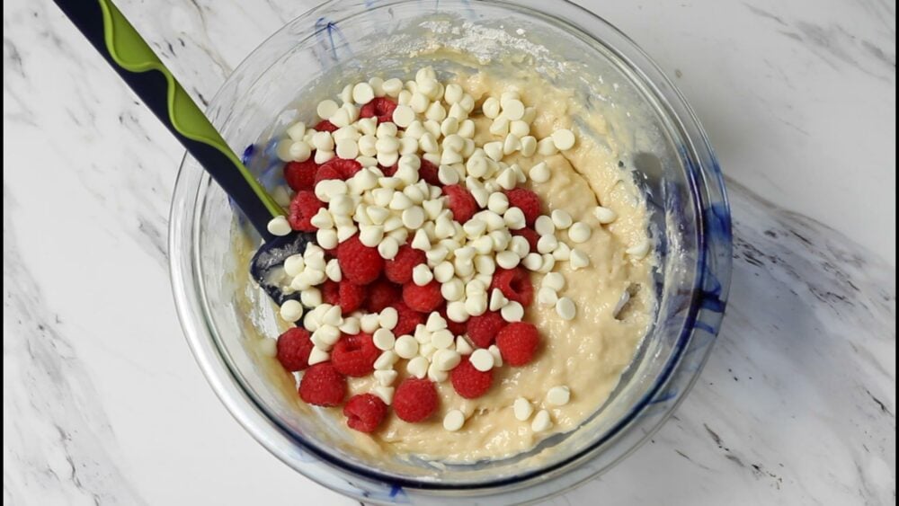 Batter, white chocolate chips, raspberries in a bowl.