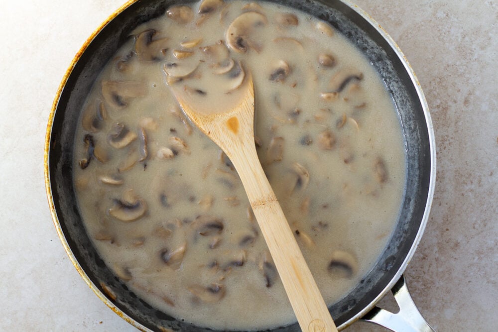 Cooked sliced mushrooms in pan with spoon.