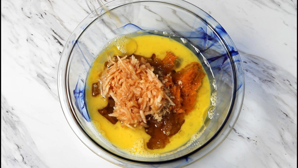 Shredded apple, whisked eggs, pumpkin puree in a bowl.