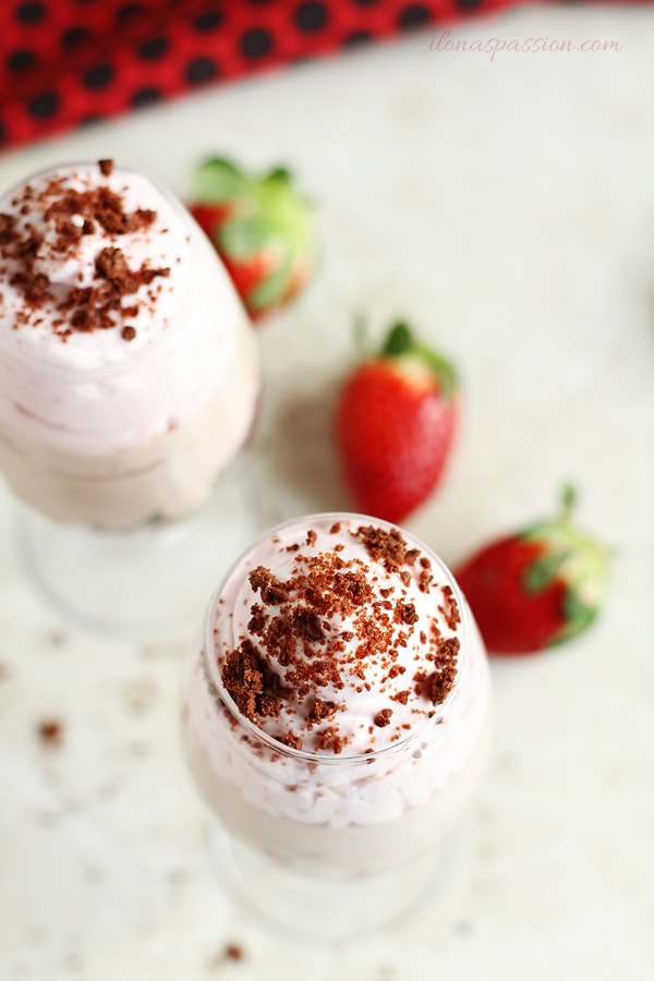 Two glasses with whipped cream mousse and fresh strawberries on the side.