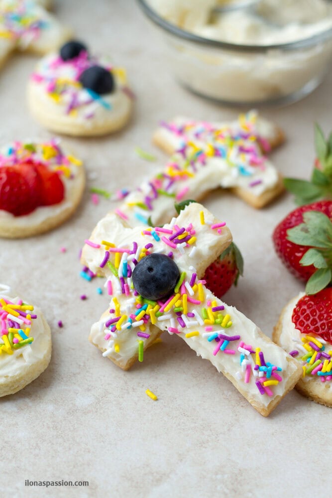 A cross shaped frosted sugar cookie with colorful sprinkles.
