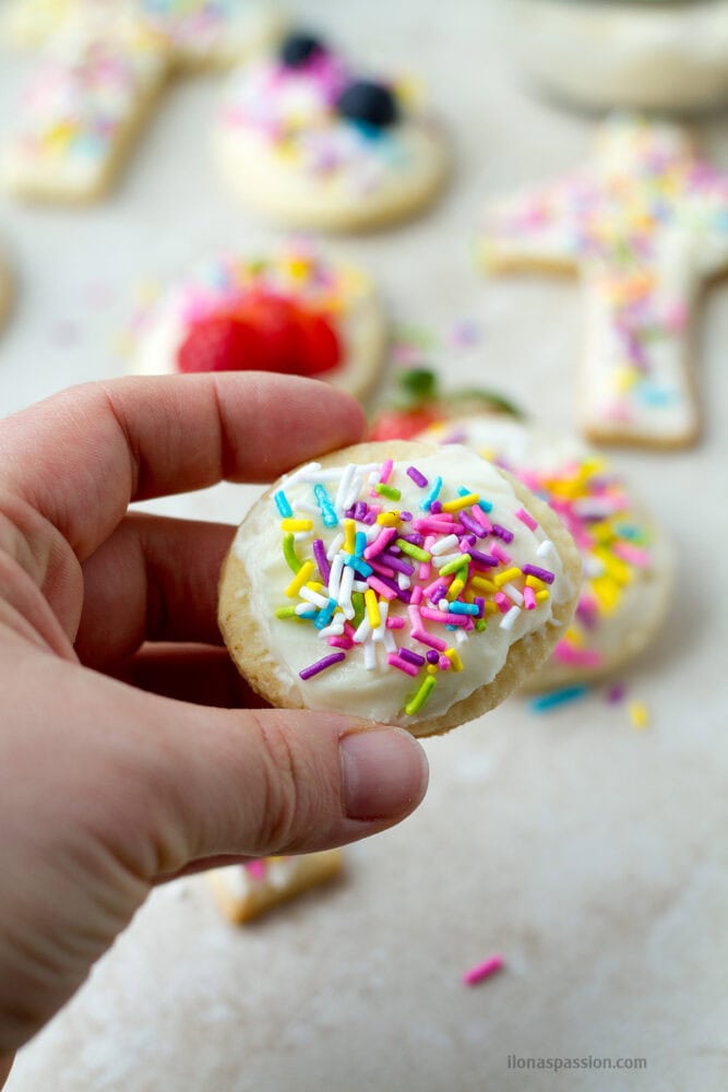 A hand holding an egg shaped frosted sugar cookie with sprinkles.