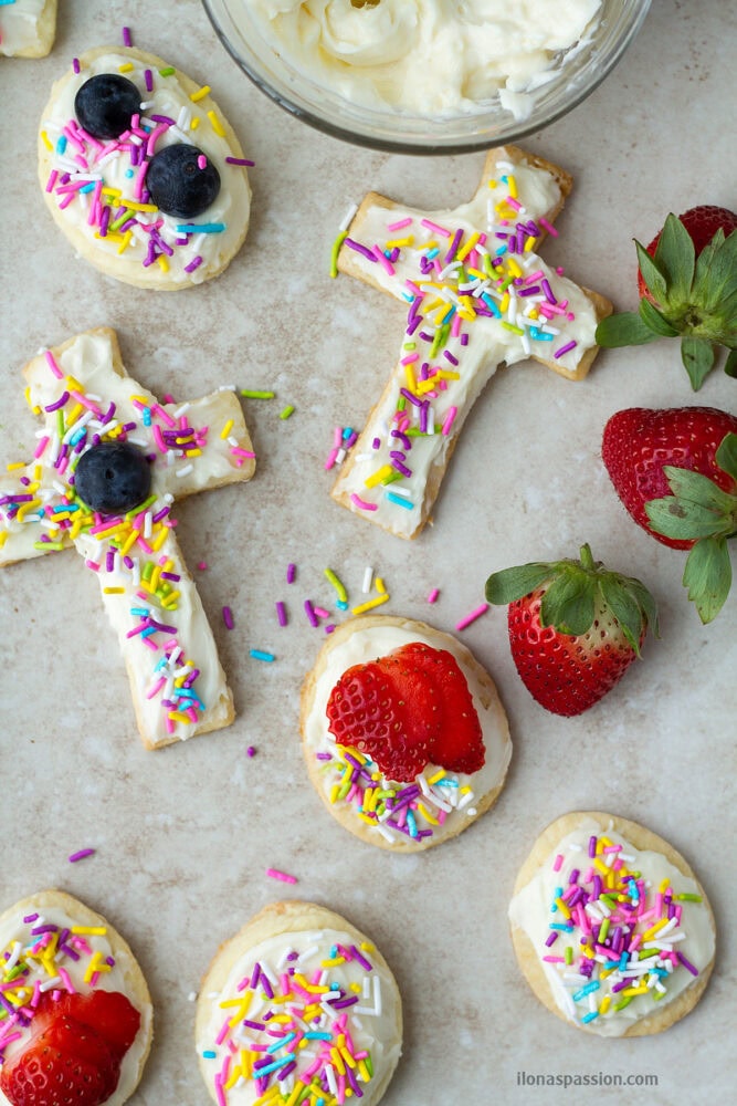Cross and egg shaped cut out cookies with sprinkles and berries.