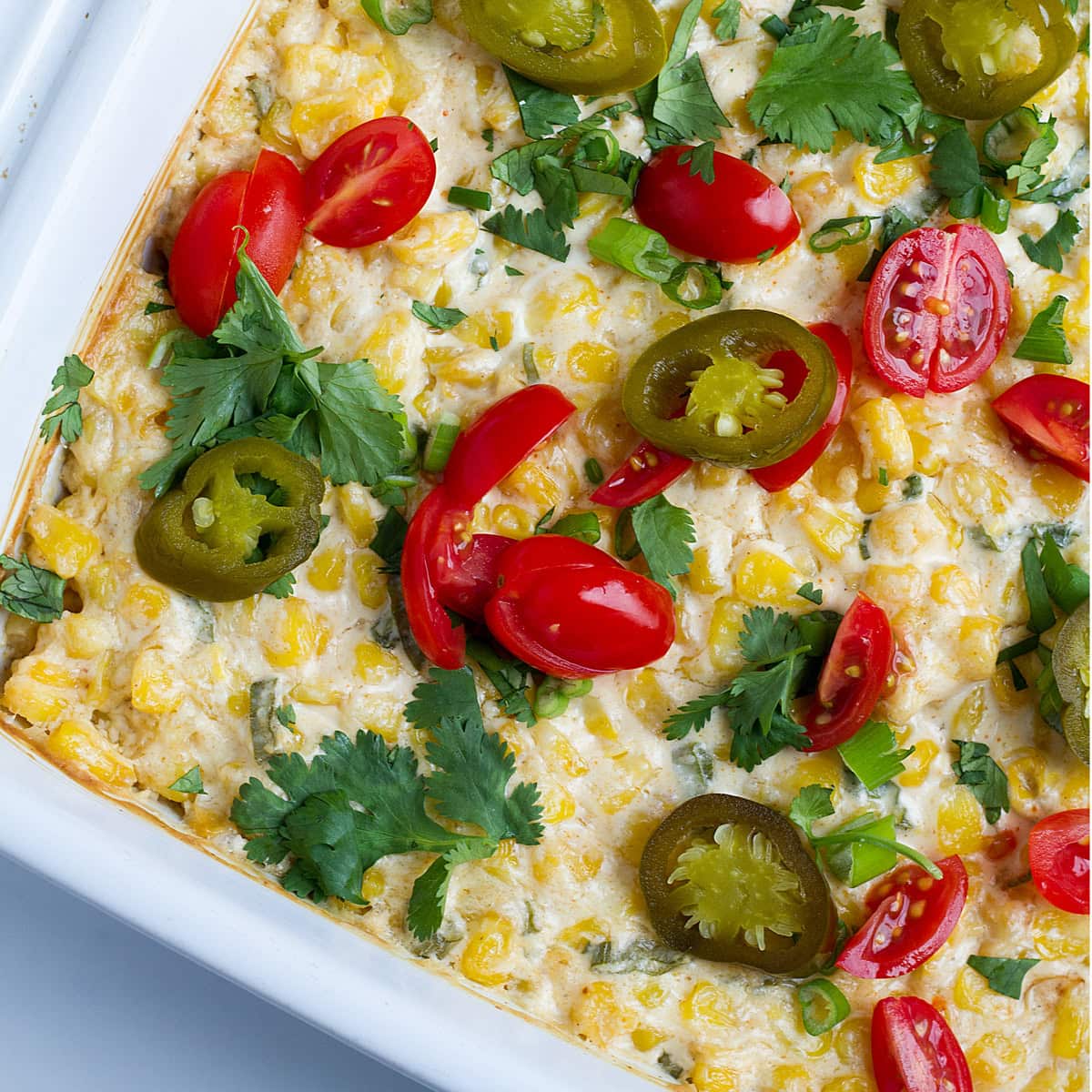 Baked cream cheese corn dip topped with cilantro, jalapeno and cocktail tomatoes.